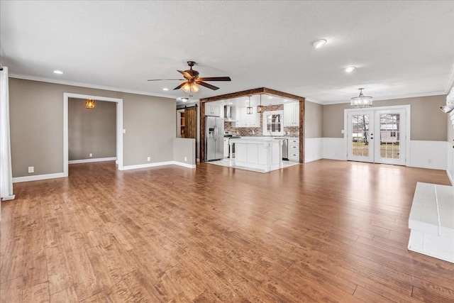 unfurnished living room featuring ceiling fan with notable chandelier, light wood-style flooring, ornamental molding, and a textured ceiling