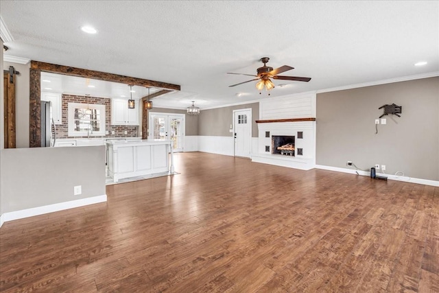 unfurnished living room featuring wood finished floors, ornamental molding, a textured ceiling, and ceiling fan