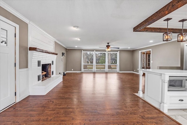 unfurnished living room with crown molding, baseboards, ceiling fan, a brick fireplace, and wood finished floors