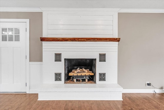 room details with ornamental molding, visible vents, a large fireplace, and wood finished floors