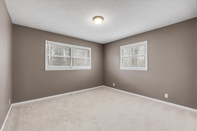 carpeted spare room with visible vents, baseboards, and a textured ceiling