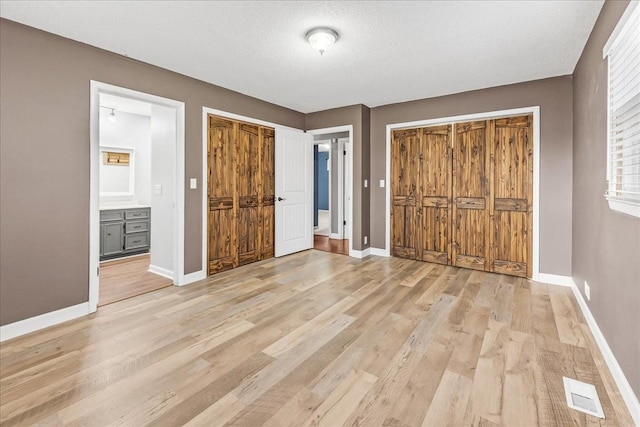 unfurnished bedroom featuring a textured ceiling, light wood-style flooring, ensuite bathroom, baseboards, and visible vents