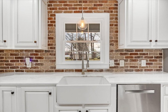kitchen featuring white cabinets, a sink, stainless steel dishwasher, and brick wall