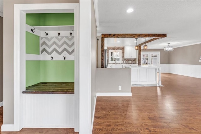 interior space with beamed ceiling, a textured ceiling, wood finished floors, and wainscoting