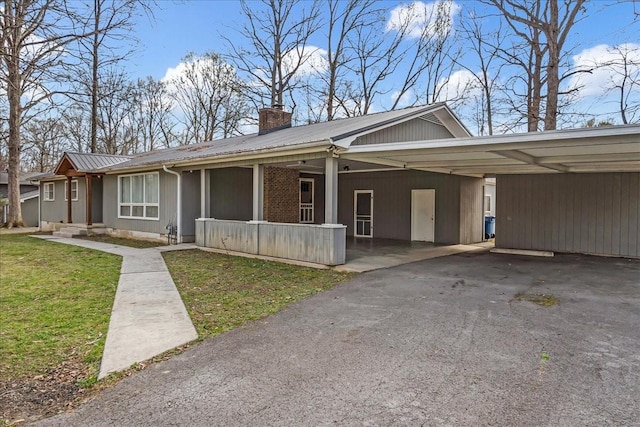view of front of house featuring metal roof, a chimney, a front lawn, driveway, and a carport