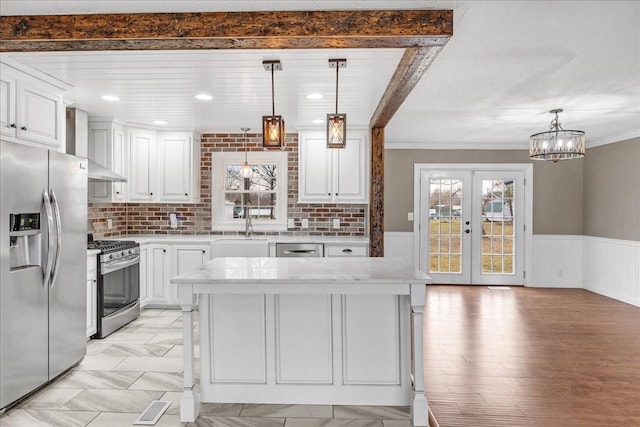 kitchen with white cabinetry, wainscoting, a sink, appliances with stainless steel finishes, and wall chimney exhaust hood