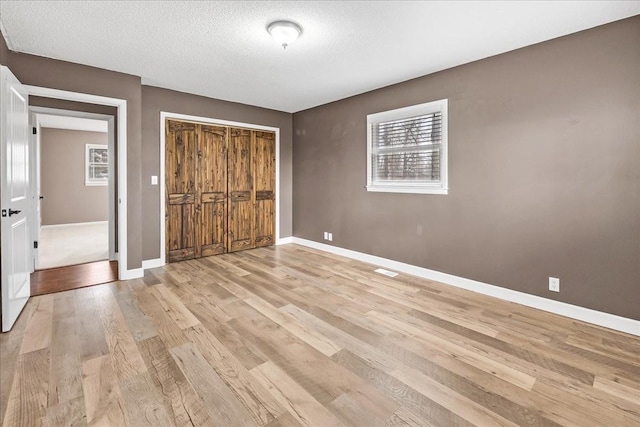 unfurnished bedroom featuring baseboards, light wood-type flooring, a closet, and a textured ceiling