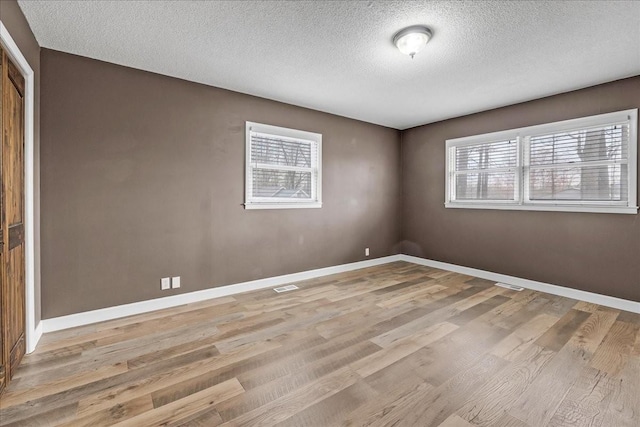 unfurnished room featuring light wood finished floors, baseboards, and a textured ceiling