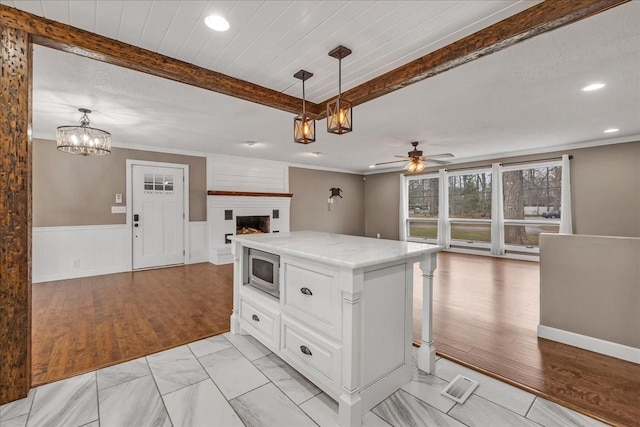 kitchen featuring stainless steel microwave, open floor plan, beamed ceiling, and wainscoting