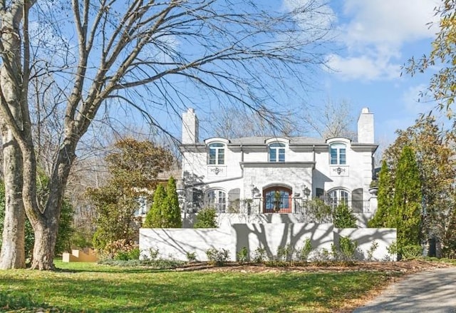 french country home featuring stone siding, a front lawn, and a chimney
