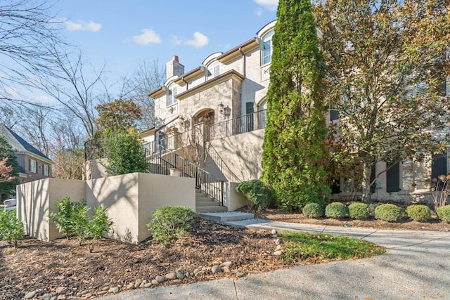 view of front of property with stucco siding, a chimney, fence, and stairway