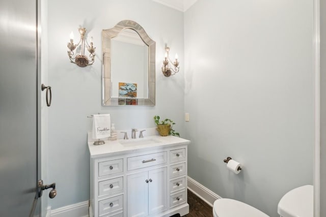 half bath with toilet, vanity, baseboards, and wood finished floors