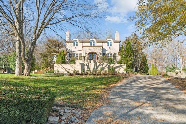 view of front facade with stucco siding, a chimney, aphalt driveway, and a front lawn