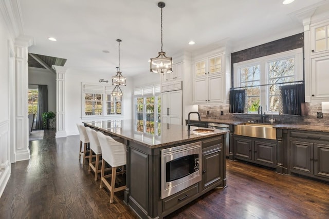 kitchen with decorative backsplash, dark wood-style flooring, appliances with stainless steel finishes, an island with sink, and a sink