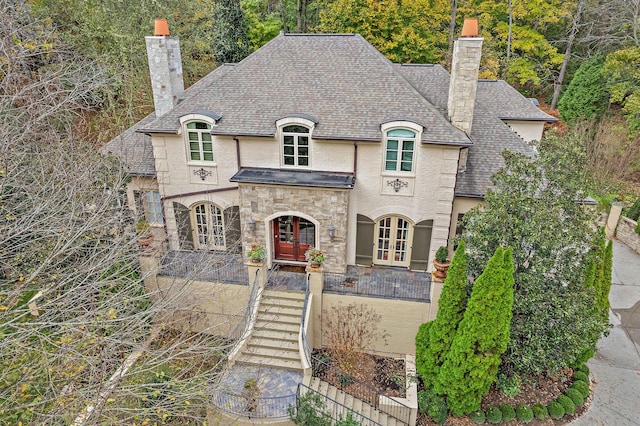 french provincial home featuring french doors, stone siding, and a chimney