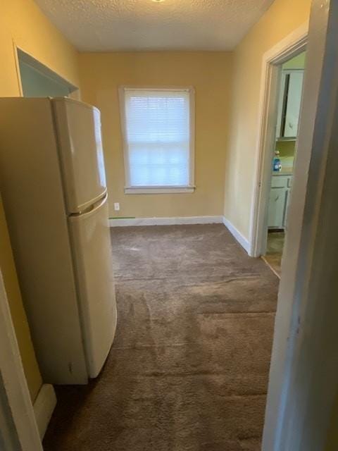 hall featuring baseboards, dark colored carpet, and a textured ceiling
