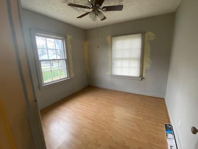 unfurnished room with a ceiling fan, baseboards, light wood-style floors, and a textured ceiling