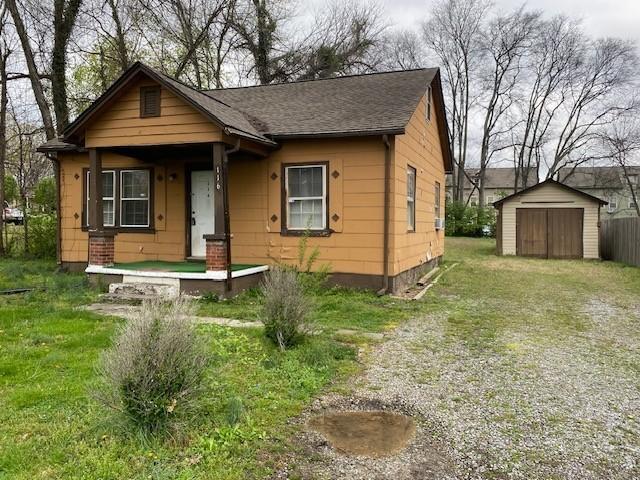 bungalow-style home with an outbuilding, driveway, a storage unit, covered porch, and a shingled roof