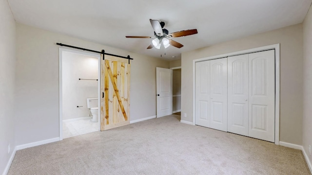 unfurnished bedroom with connected bathroom, a closet, a barn door, baseboards, and carpet