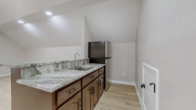 kitchen featuring light countertops, baseboards, lofted ceiling, a sink, and light wood-type flooring