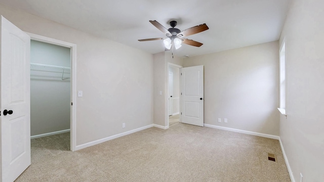 unfurnished bedroom with carpet flooring, a walk in closet, baseboards, and visible vents