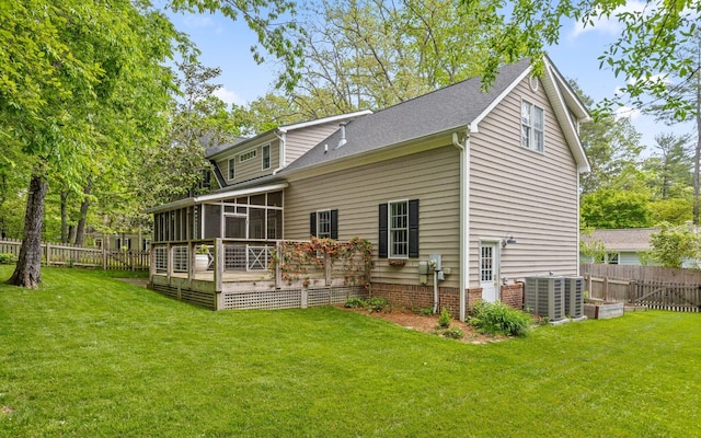 back of property featuring a fenced backyard, a yard, central AC unit, and a sunroom
