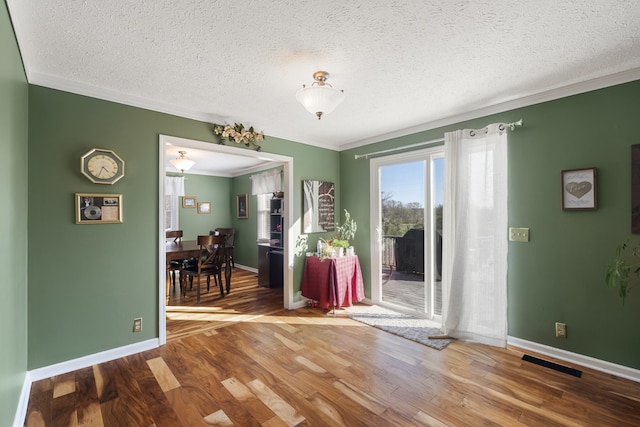 interior space with visible vents, wood finished floors, ornamental molding, and a textured ceiling