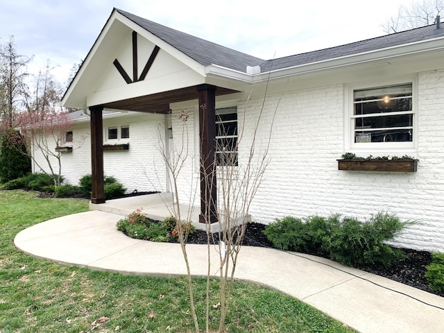 entrance to property with a shingled roof, brick siding, and a yard