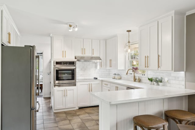 kitchen with backsplash, under cabinet range hood, a sink, and stainless steel appliances