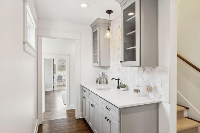 bar featuring baseboards, tasteful backsplash, dark wood finished floors, a sink, and decorative light fixtures