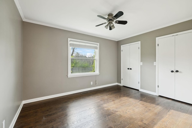 unfurnished bedroom with two closets, crown molding, baseboards, visible vents, and wood finished floors