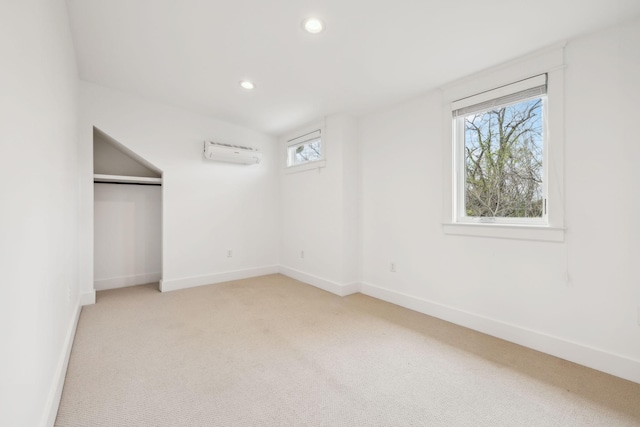 unfurnished bedroom with a closet, a wall mounted AC, baseboards, light colored carpet, and recessed lighting