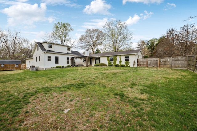 rear view of house featuring cooling unit, a chimney, fence, and a lawn