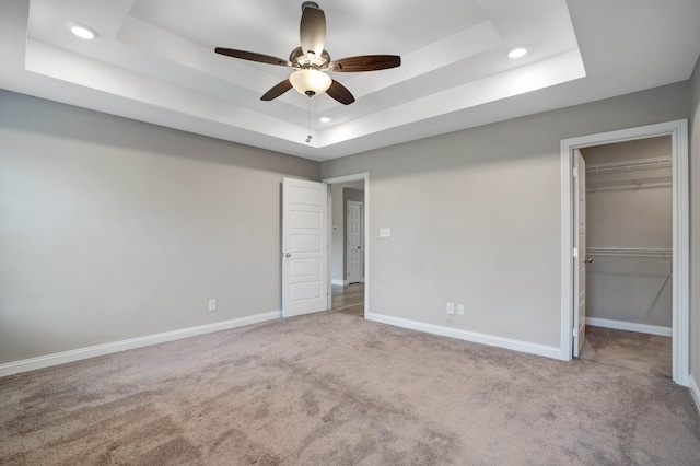unfurnished bedroom with baseboards, carpet flooring, a spacious closet, and a raised ceiling