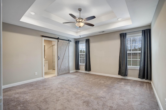 unfurnished room with baseboards, ceiling fan, a barn door, carpet floors, and a tray ceiling