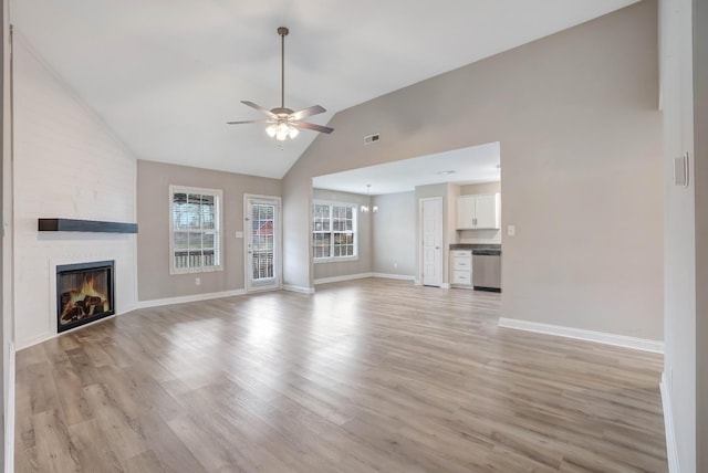 unfurnished living room with ceiling fan with notable chandelier, light wood-style floors, baseboards, and a large fireplace