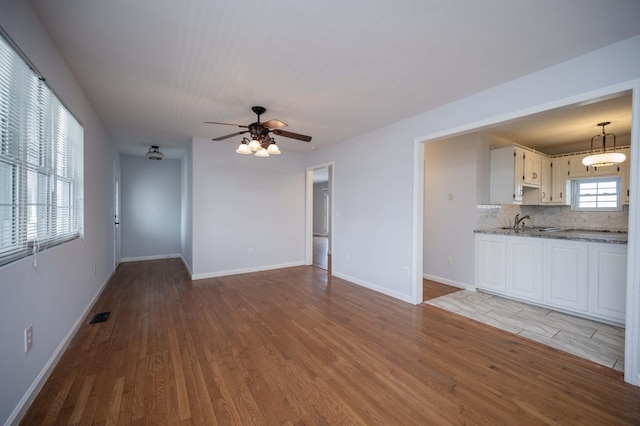 unfurnished living room featuring a sink, wood finished floors, baseboards, visible vents, and ceiling fan