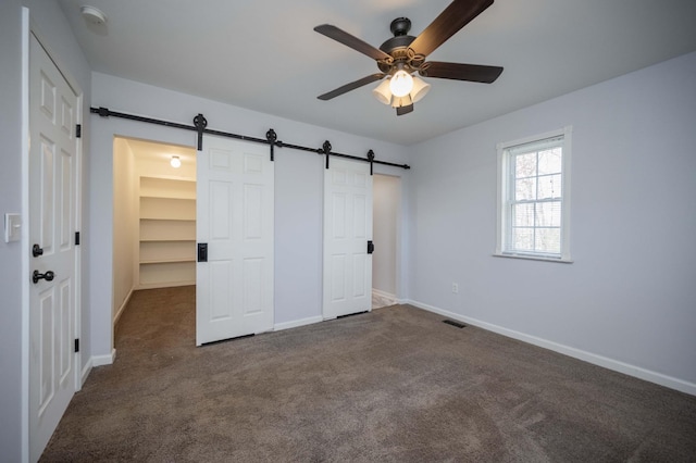 unfurnished bedroom featuring dark carpet, a barn door, visible vents, and baseboards