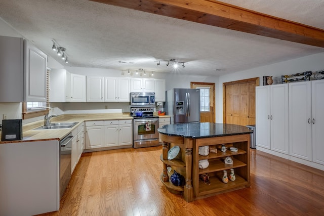 kitchen featuring a textured ceiling, light wood-style flooring, stainless steel appliances, a sink, and open shelves