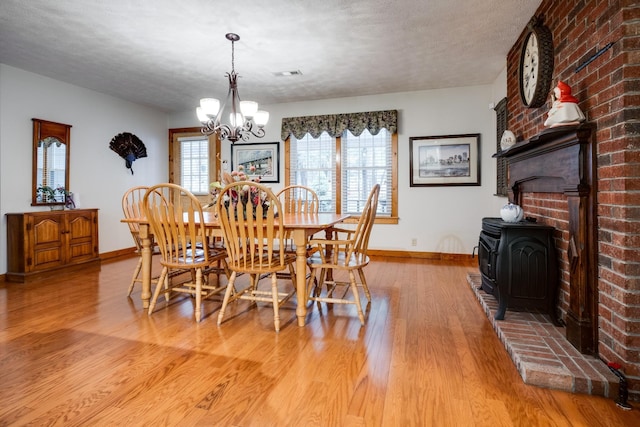 dining area featuring a wood stove, baseboards, a textured ceiling, light wood-style floors, and a notable chandelier