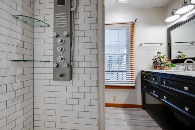 bathroom with vanity, baseboards, tiled shower, and wood finished floors