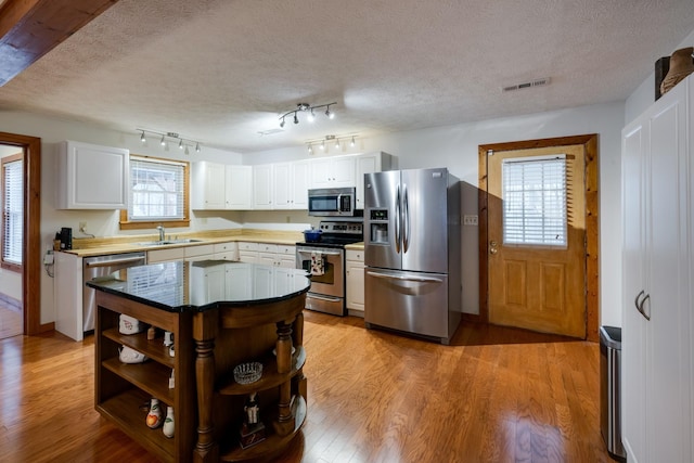 kitchen with open shelves, light wood-type flooring, a sink, visible vents, and appliances with stainless steel finishes