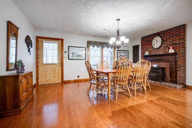 dining area featuring a textured ceiling, baseboards, wood finished floors, an inviting chandelier, and a wood stove