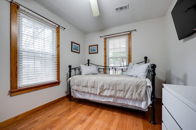 bedroom with a ceiling fan, a textured ceiling, baseboards, visible vents, and light wood-style floors