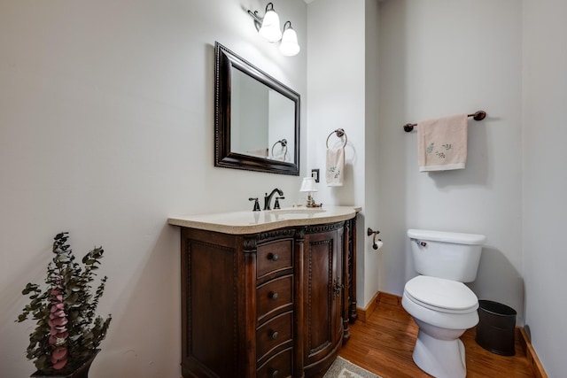 bathroom with baseboards, wood finished floors, toilet, and vanity