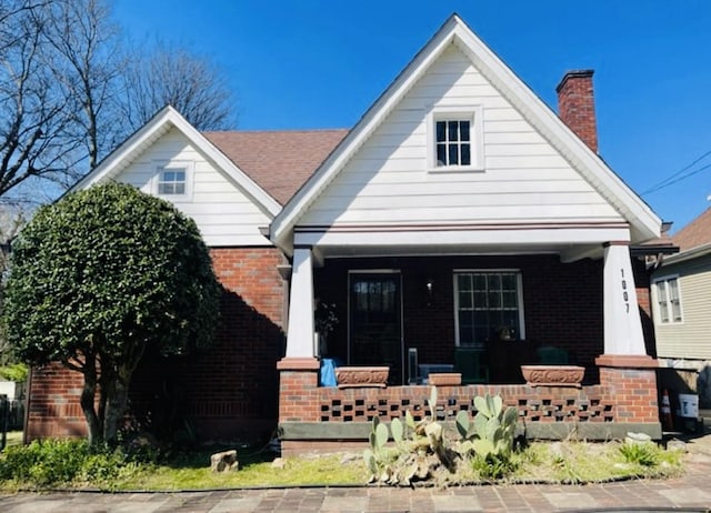 view of front of property featuring a chimney, a porch, and brick siding