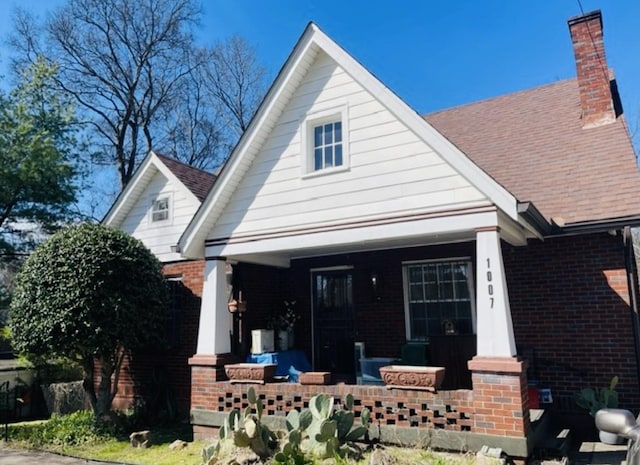 view of front of property with a chimney, covered porch, and brick siding