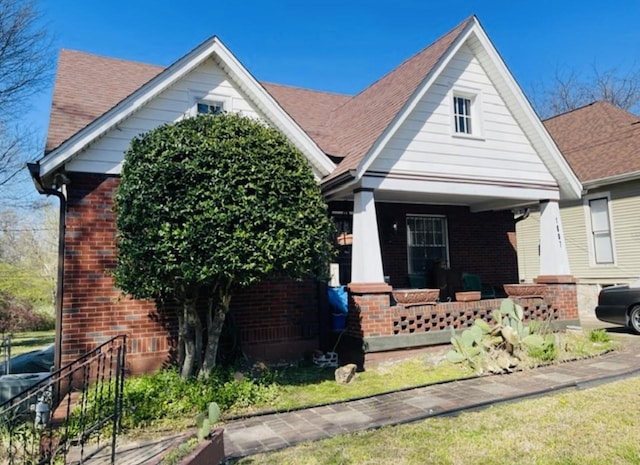 view of front of home with covered porch, brick siding, and roof with shingles