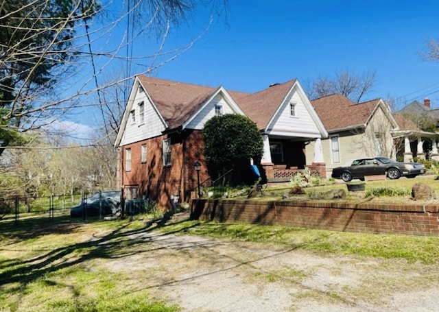 view of front of home with driveway, covered porch, fence, brick siding, and a front lawn