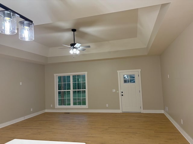 foyer entrance featuring a ceiling fan, baseboards, a raised ceiling, and light wood-style floors